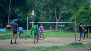 ANG THAILAND - 9 HAZİRAN 2019 Taylandlı gençler parkta sepak oynuyorlar. Yerel yerleşim bölgesindeki yeşil ağaçlara karşı voleybol oynayan bir grup adam. Geleneksel ulusal spor oyunu.