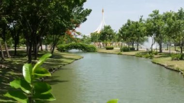 BANGKOK, THAILAND - 12 HAZİRAN, 2019: parktaki pavyonun yanındaki çiçek açan bahçe. Kral Rama IX Parkı 'nda güneşli bir günde, bulutsuz mavi gökyüzü karşısında yeşil ağaçlar ve çiçekler büyüyor.