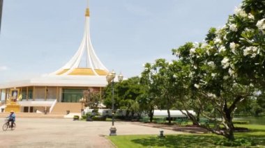 BANGKOK, THAILAND - 12 HAZİRAN, 2019: parktaki pavyonun yanındaki çiçek açan bahçe. Kral Rama IX Parkı 'nda güneşli bir günde, bulutsuz mavi gökyüzü karşısında yeşil ağaçlar ve çiçekler büyüyor.