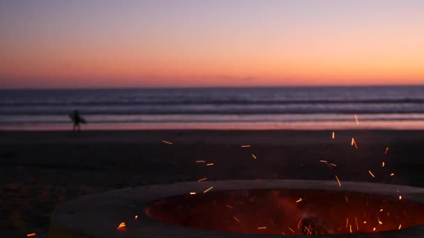 Ognisko w Kalifornii USA. Obóz ognisko na plaży o zmierzchu ocean, ognisko płomień, surfer i fale. — Wideo stockowe