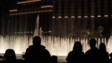 LAS VEGAS, NEVADA USA - 13 Aralık 2019: İnsanlar geceleri Bellagio Fountain müzik performansına bakıyor. Karşıt siluetler ve parlayan dans eden su sıçramaları. Kumar şehrinde eğlence şovu.