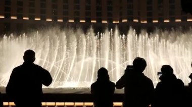 LAS VEGAS, NEVADA USA - 13 Aralık 2019: İnsanlar geceleri Bellagio Fountain müzik performansına bakıyor. Karşıt siluetler ve parlayan dans eden su sıçramaları. Kumar şehrinde eğlence şovu.