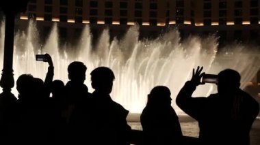 LAS VEGAS, NEVADA USA - 13 Aralık 2019: İnsanlar geceleri Bellagio Fountain müzik performansına bakıyor. Karşıt siluetler ve parlayan dans eden su sıçramaları. Kumar şehrinde eğlence şovu.