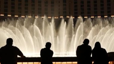 LAS VEGAS, NEVADA USA - 13 Aralık 2019: İnsanlar geceleri Bellagio Fountain müzik performansına bakıyor. Karşıt siluetler ve parlayan dans eden su sıçramaları. Kumar şehrinde eğlence şovu.