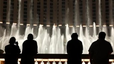 LAS VEGAS, NEVADA USA - 13 Aralık 2019: İnsanlar geceleri Bellagio Fountain müzik performansına bakıyor. Karşıt siluetler ve parlayan dans eden su sıçramaları. Kumar şehrinde eğlence şovu.