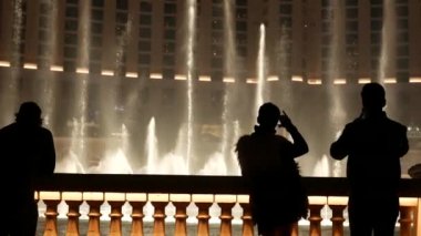 LAS VEGAS, NEVADA USA - 13 Aralık 2019: İnsanlar geceleri Bellagio Fountain müzik performansına bakıyor. Karşıt siluetler ve parlayan dans eden su sıçramaları. Kumar şehrinde eğlence şovu.