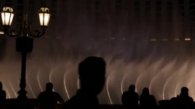 LAS VEGAS, NEVADA USA - 13 Aralık 2019: İnsanlar geceleri Bellagio Fountain müzik performansına bakıyor. Karşıt siluetler ve parlayan dans eden su sıçramaları. Kumar şehrinde eğlence şovu.