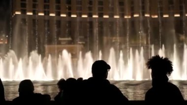 LAS VEGAS, NEVADA USA - 13 Aralık 2019: İnsanlar geceleri Bellagio Fountain müzik performansına bakıyor. Karşıt siluetler ve parlayan dans eden su sıçramaları. Kumar şehrinde eğlence şovu.