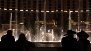 LAS VEGAS, NEVADA USA - 13 Aralık 2019: İnsanlar geceleri Bellagio Fountain müzik performansına bakıyor. Karşıt siluetler ve parlayan dans eden su sıçramaları. Kumar şehrinde eğlence şovu.
