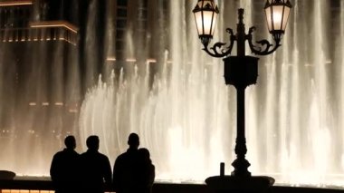 LAS VEGAS, NEVADA USA - 13 Aralık 2019: İnsanlar geceleri Bellagio Fountain müzik performansına bakıyor. Karşıt siluetler ve parlayan dans eden su sıçramaları. Kumar şehrinde eğlence şovu.