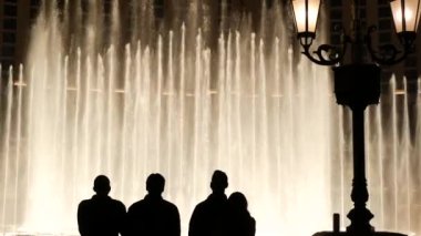 LAS VEGAS, NEVADA USA - 13 Aralık 2019: İnsanlar geceleri Bellagio Fountain müzik performansına bakıyor. Karşıt siluetler ve parlayan dans eden su sıçramaları. Kumar şehrinde eğlence şovu.