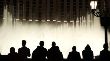 LAS VEGAS, NEVADA USA - 13 Aralık 2019: İnsanlar geceleri Bellagio Fountain müzik performansına bakıyor. Karşıt siluetler ve parlayan dans eden su sıçramaları. Kumar şehrinde eğlence şovu.