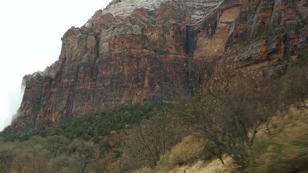 Road trip, driving auto in Zion Canyon, Utah, USA. Hitchhiking traveling in America, autumn journey. Red alien steep cliffs, rain and bare trees. Foggy weather and calm fall atmosphere. View from car — Stock Photo, Image