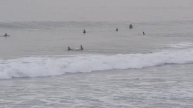 Encinitas, California USA - 21 Aralık 2019: İnsanlar soğuk okyanus suyunda sörf yapıyor. Sörf yapan sörfçüler, sörf tahtasında durup deniz dalgalarını yakalıyorlar. Su sporları hobisi, sisli kış havası. Sağlıklı yaşam tarzı