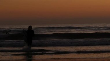 Okyanus Kenarı, Kaliforniya ABD - 16 Şubat 2020: Sörfçü silueti, Pasifik Okyanus Sahili, su dalgaları ve gün batımı. Tropik sahil şeridi, sahil tatil beldesi. İnsanlar spor olsun diye sörf yapmaktan hoşlanıyor..