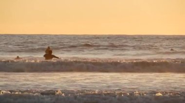 Okyanus Kenarı, Kaliforniya ABD - 27 Aralık 2019: Sörfçü silueti, Pasifik Okyanus Sahili, su dalgaları ve gün batımı. Tropik sahil şeridi, sahil tatil beldesi. İnsanlar spor olsun diye sörf yapmaktan hoşlanıyor..