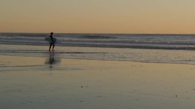 Okyanus Kenarı, Kaliforniya ABD - 27 Aralık 2019: Sörfçü silueti, Pasifik Okyanus Sahili, su dalgaları ve gün batımı. Tropik sahil şeridi, sahil tatil beldesi. İnsanlar spor olsun diye sörf yapmaktan hoşlanıyor..