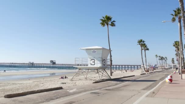 美国加利福尼亚海洋 2020年2月8日 人们步行 码头附近的海滨长廊 太平洋热带海滩旅游胜地 有棕榈树 救生塔 坐轮椅的老年残疾人 — 图库视频影像