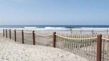 Encinitas, California USA - 23 Şubat 2020: Pasifik kıyıları, insanlar deniz dalgaları ile okyanus sahillerinde yürüyorlar. San Diego ve Los Angeles yakınlarındaki kumlu sahilde çitlerle kıyı girişi. Köpek sahipleri.