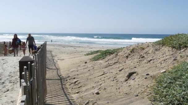 Encinitas, Kalifornie USA - 23. února 2020: Pobřeží Tichého oceánu, lidé procházející se po pláži u mořských vln. Pobřežní přístup s laťkovým plotem, rodina na písečném pobřeží v blízkosti San Diega a Los Angeles.
