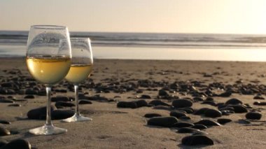 Okyanus sahilinde iki şarap bardağı. Romantik randevu için beyaz şarap bardakları, deniz suyu. Gün batımı dalgaları.