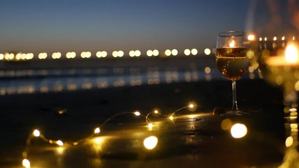 Candle flame lights in glass, romantic beach date by ocean waves, summer sea. Candlelight on sand.