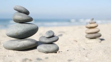 Okyanus sahilinde dengelenen kayalar, deniz dalgalarıyla istiflenen taşlar. Kumlu sahilde çakıl taşı piramidi