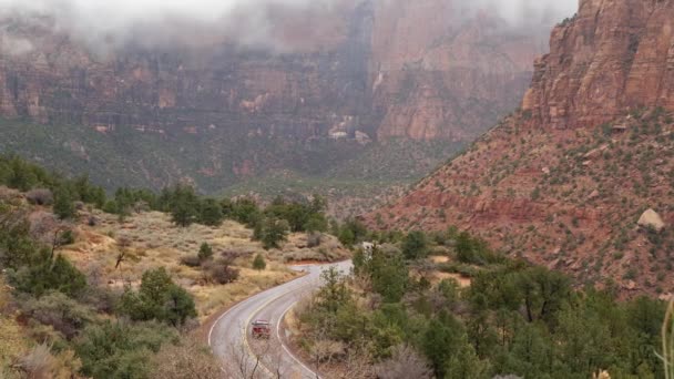 Red steep cliffs in Zion Canyon, Utah, USA. Hitchhiking trip, traveling in America, autumn journey. Rain, rocks and bare trees. Foggy weather and calm fall atmosphere. Road with yellow dividing line — Stock Video