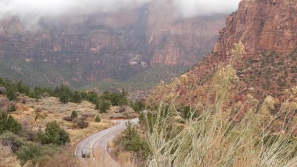 Falaises escarpées rouges à Zion Canyon, Utah, États-Unis. Voyage en auto-stop, voyage en Amérique, voyage d'automne. Pluie, rochers et arbres nus. Météo brumeuse et atmosphère d'automne calme. Route avec ligne de démarcation jaune — Video