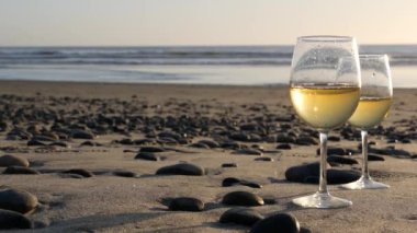 Okyanus sahilinde iki şarap bardağı. Romantik randevu için beyaz şarap bardakları, deniz suyu. Gün batımı dalgaları.