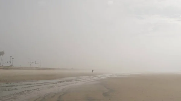 Sandy misty beach California USA. Pacific ocean coast dense fog on sea shore. Milky smog brume haze