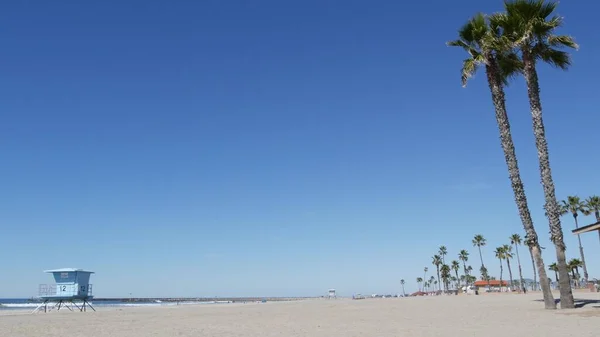 Palmy na bílé písečné pláži, oceánské pobřeží v Kalifornii USA. Záchranná věž, chata na strážní věži. — Stock fotografie