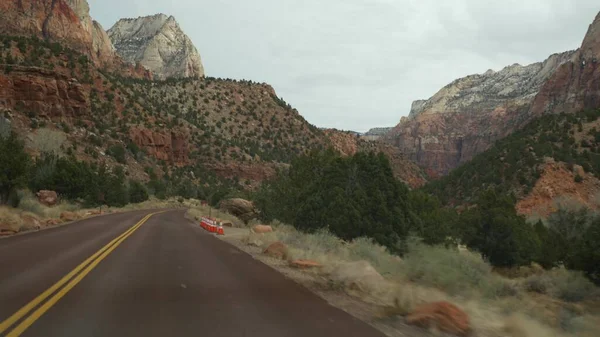 Road trip, driving auto in Zion Canyon, Utah, USA. Hitchhiking traveling in America, autumn journey. Red alien steep cliffs, rain and bare trees. Foggy weather and calm fall atmosphere. View from car