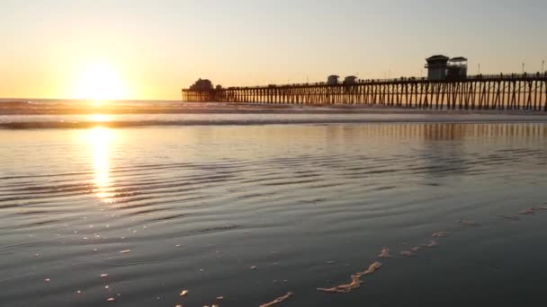 Houten pier op palen, silhouet bij zonsondergang, Californië USA, Oceanside. Zonnige zee golven bij zonsondergang. — Stockvideo