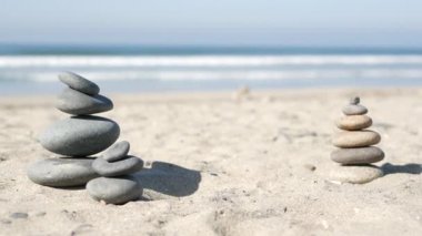 Okyanus sahilinde dengelenen kayalar, deniz dalgalarıyla istiflenen taşlar. Kumlu sahilde çakıl taşı piramidi