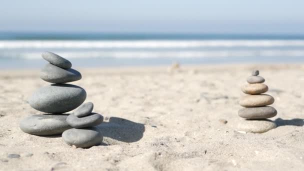 Скеля балансує на океанському пляжі, камені, що укладаються морськими хвилями води. Піраміда з гальки на піщаному березі — стокове відео