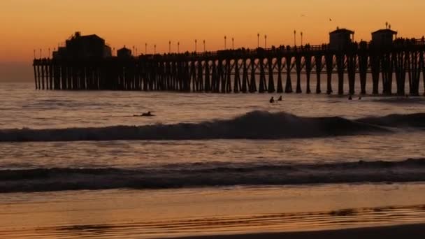 Pier silhouet bij zonsondergang, Californië USA, Oceanside. Surf resort, oceaan tropisch strand. Surfer wacht op golf. — Stockvideo