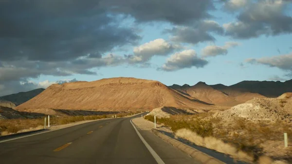 Viaje por carretera, conduciendo auto desde Death Valley a Las Vegas, Nevada, EE.UU. Hacer autostop viajando por América. Viaje por carretera, atmósfera dramática, montaña al atardecer y desierto de Mojave. Vista desde el coche —  Fotos de Stock