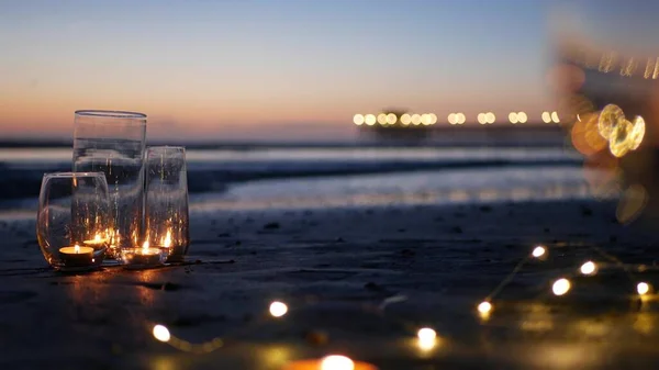 Κεριά φώτα φλόγας σε γυαλί, ρομαντική ημερομηνία παραλία από κύματα του ωκεανού, τη θάλασσα του καλοκαιριού. Φως κεριών στην άμμο. — Φωτογραφία Αρχείου