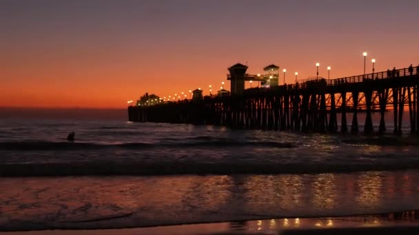 Silueta de muelle al atardecer, California USA, Oceanside. Surf resort, playa tropical oceánica. Surfista esperando ola. — Vídeo de stock