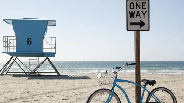Bicycle cruiser bike by ocean beach, California coast USA. Summer cycle, lifeguard tower, road sign