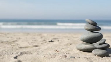 Okyanus sahilinde dengelenen kayalar, deniz dalgalarıyla istiflenen taşlar. Kumlu sahilde çakıl taşı piramidi