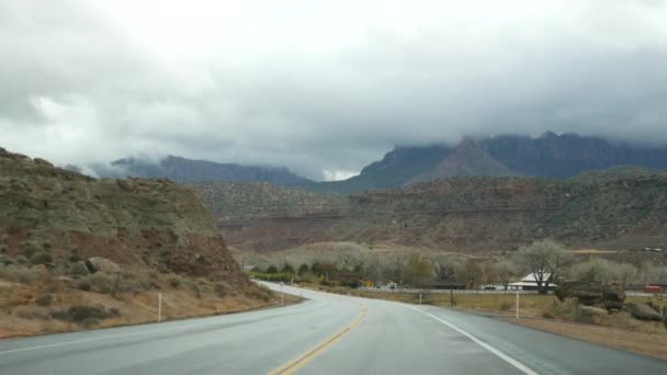 Výlet autem v Zion Canyon, Utah, USA. Stopování v Americe, podzimní cesta. Červené cizí strmé útesy, déšť a holé stromy. Mlhavé počasí a klidná podzimní atmosféra. Pohled z auta — Stock video