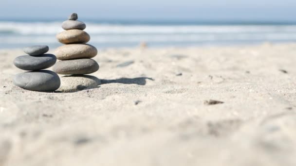 Stenen balanceren op het strand van de oceaan, stenen stapelen zich op door golven van zeewater. Piramide van kiezelsteentjes op zandstrand — Stockvideo