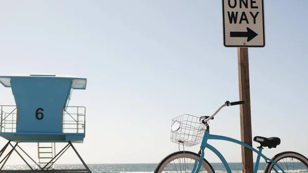 Bicycle cruiser bike by ocean beach, California coast USA. Summer cycle, lifeguard tower, road sign