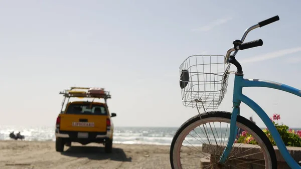 Bicycle cruiser bike by ocean beach, California coast USA. Summer cycle, lifeguard car pick up truck