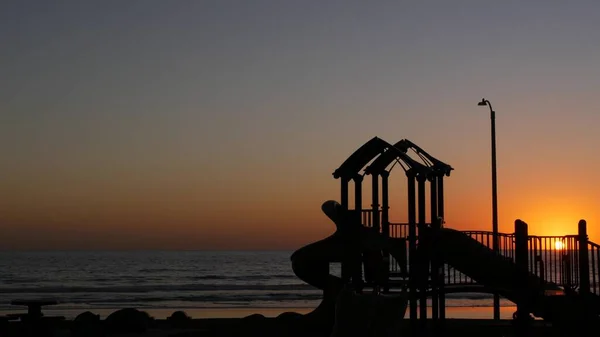 Waterfront kids playground silhouette. Children slide, beachfront recreation area. California USA — Stock Photo, Image