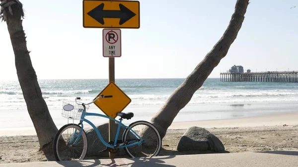 Bicycle cruiser bike by ocean beach, California coast USA. Summer cycle, road sign, waves and pier.