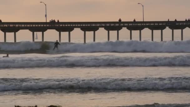 カリフォルニア州サンディエゴ 2020年11月21日 日没の山の上でオーシャンビーチ桟橋でサーフィンする人々 波のサーフボード上のサーファー 太平洋岸や海岸での休暇 レクリエーションスポーツ趣味 — ストック動画