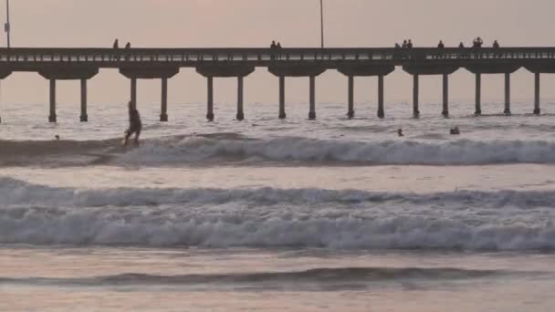 カリフォルニア州サンディエゴ 2020年11月21日 日没の山の上でオーシャンビーチ桟橋でサーフィンする人々 波のサーフボード上のサーファー 太平洋岸や海岸での休暇 レクリエーションスポーツ趣味 — ストック動画